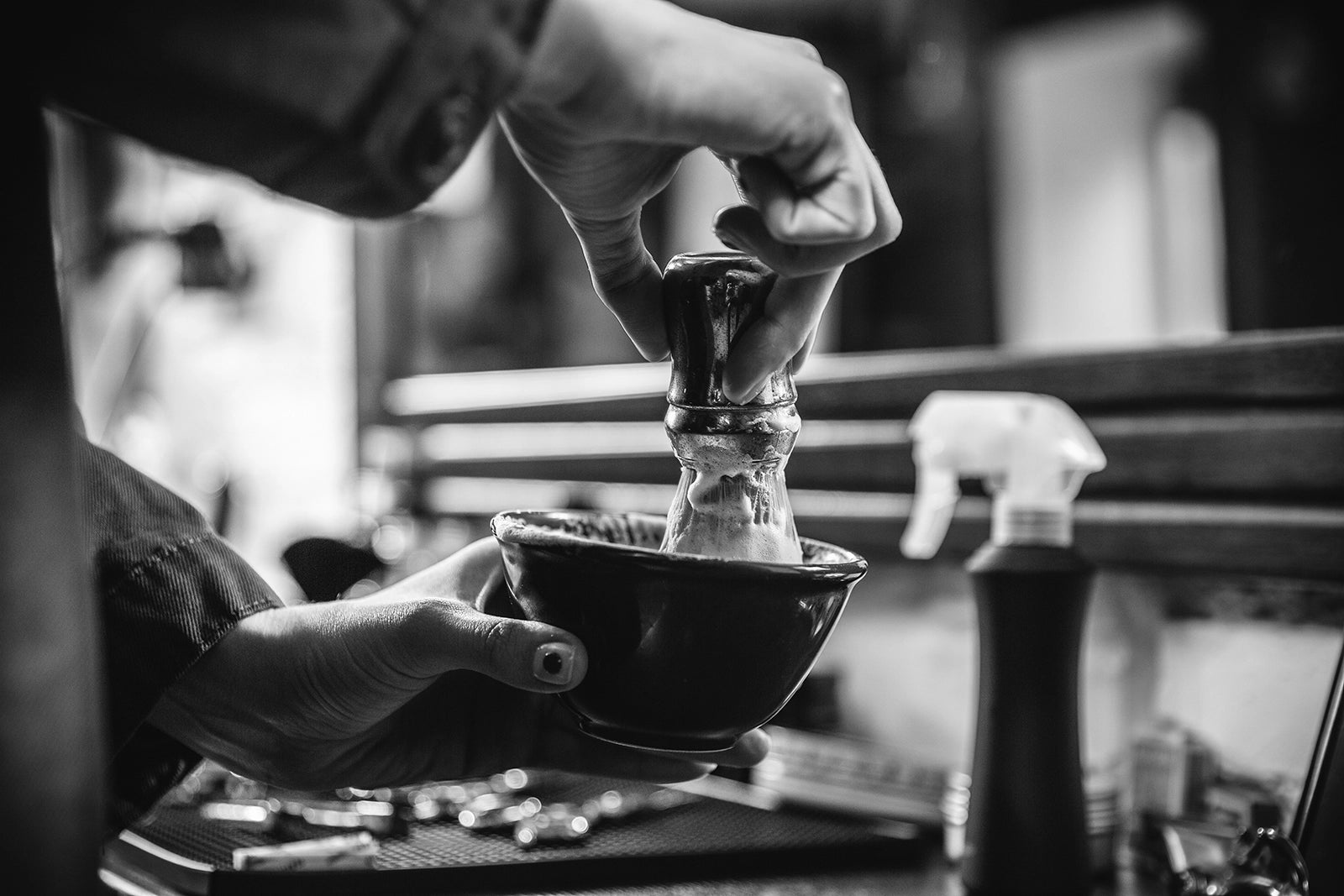 Rasierschaum in einer Rasierschüssel aufgeschlagen vor einem Spiegel im Barbershop-Ambiente – klassische Rasurpflege mit professionellem Flair.